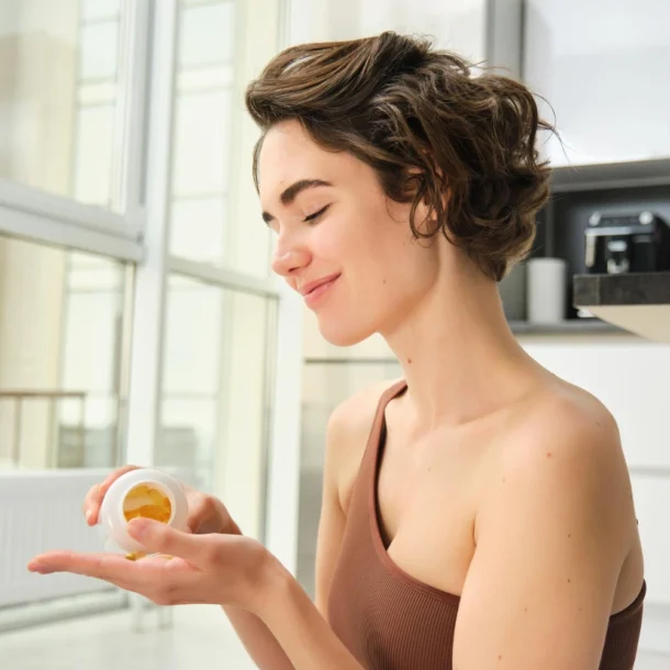 kobieta trzyma opakowanie suplementu diety i wysypuje kapsułki na rękę.